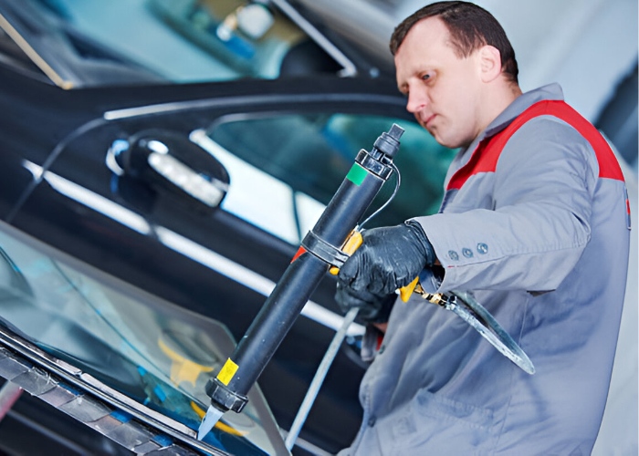 Technician applying adhesive to a vehicle windshield using a specialized glue gun during a windshield replacement.