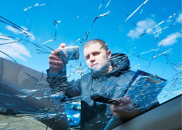 Technician examining a shattered windshield, showing extensive cracks across the glass, ready for windshield replacement service.