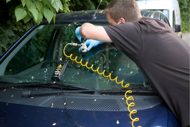 Technician repairing a car windshield outdoors using specialized equipment as part of mobile glass services.